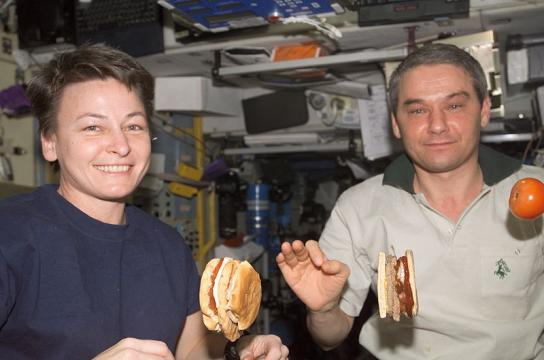 ISS astronauts eating a meal in the Service Module with tomato and hamburger floating (Image credit – NASA, Wikimedia Commons)